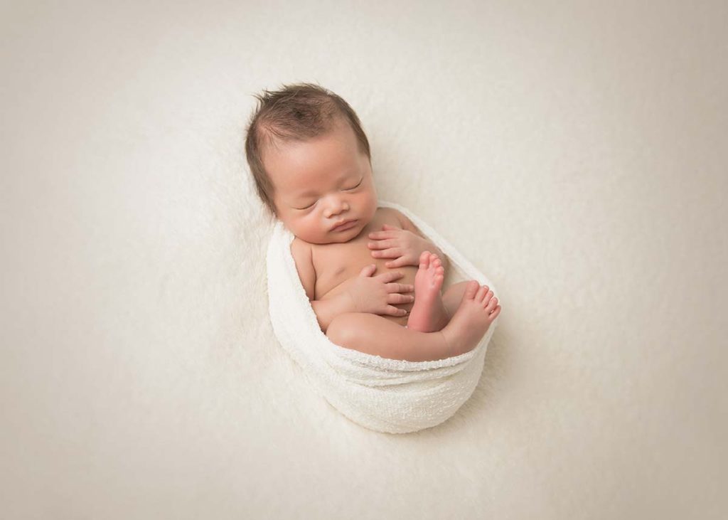 Cozy infant sleeping in a warp and posing for a newborn photographer in Connecticut.