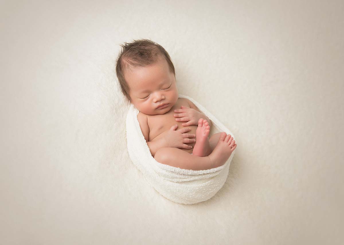Cozy infant sleeping in a warp and posing for a newborn photographer in Denver