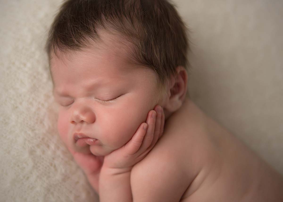 Newborn baby sleeping with his hands on cheeks in this timeless newborn photo.