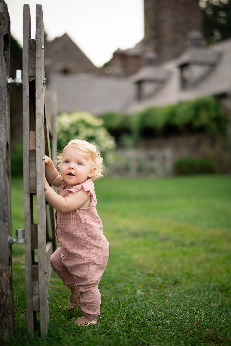 Baby in overalls climbing a wooden gate at a Colorado farm