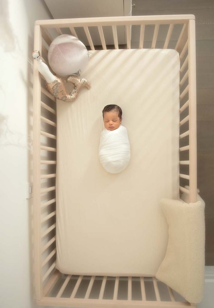 Newborn wrapped in a swaddle sleeping in a crib at a house in Greenwich CT.