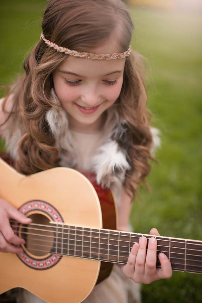 Beautiful girl in a fur vest and a headband playing a guitar