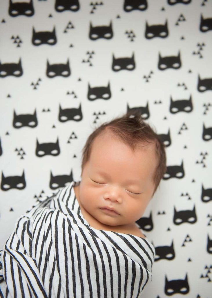 Batman sheets in a crib with a sleepy newborn baby