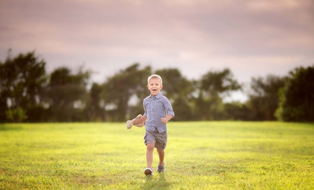 Happy boy in shorts running through a field in Stamford CT while holding his stuffed animal