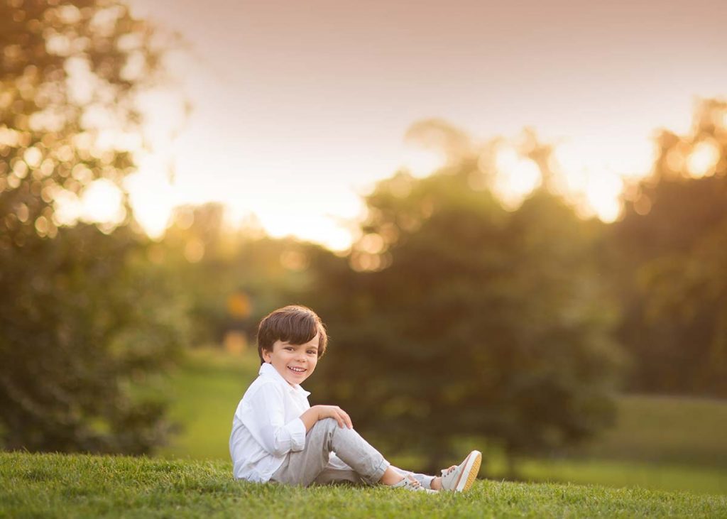 Young boy in a white shirt sitting in a park during sunset