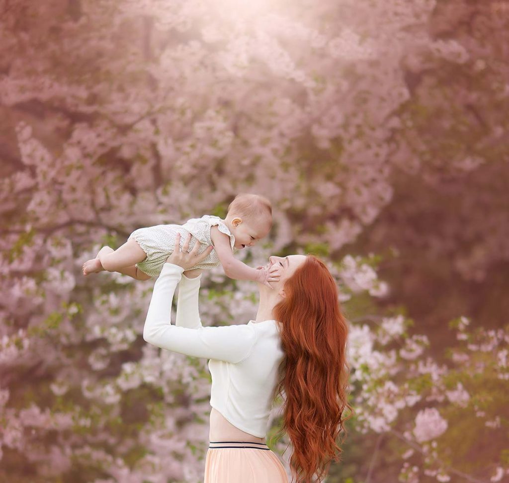 Mother with red hair holding her pretty baby amidst cherry blossoms