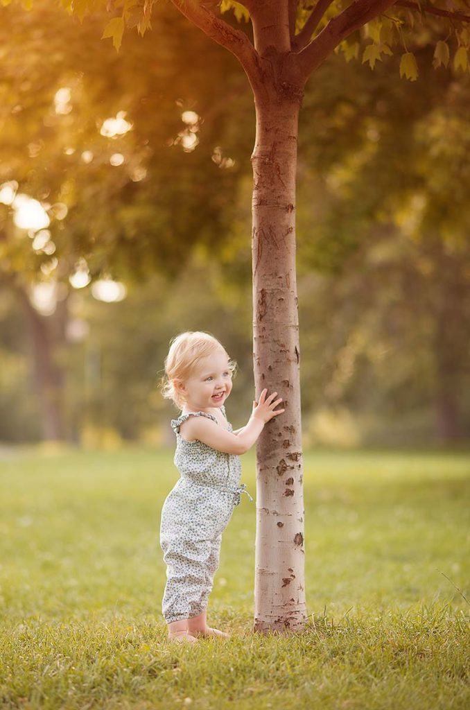 Cute baby girl holding a tree trunk
