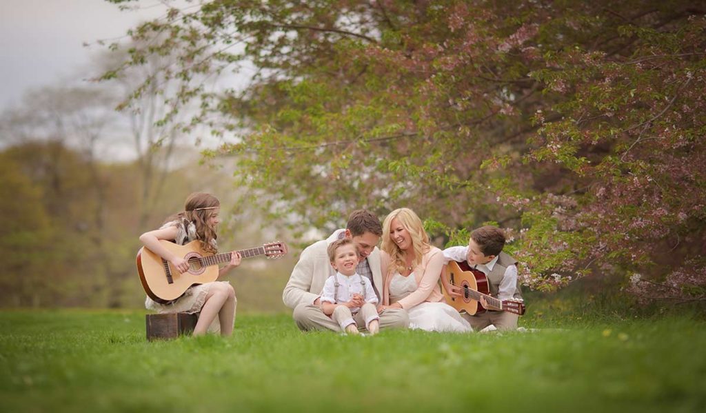 A stylish family sharing a picnic in a park with children playing guitars in a park in Connecticut.