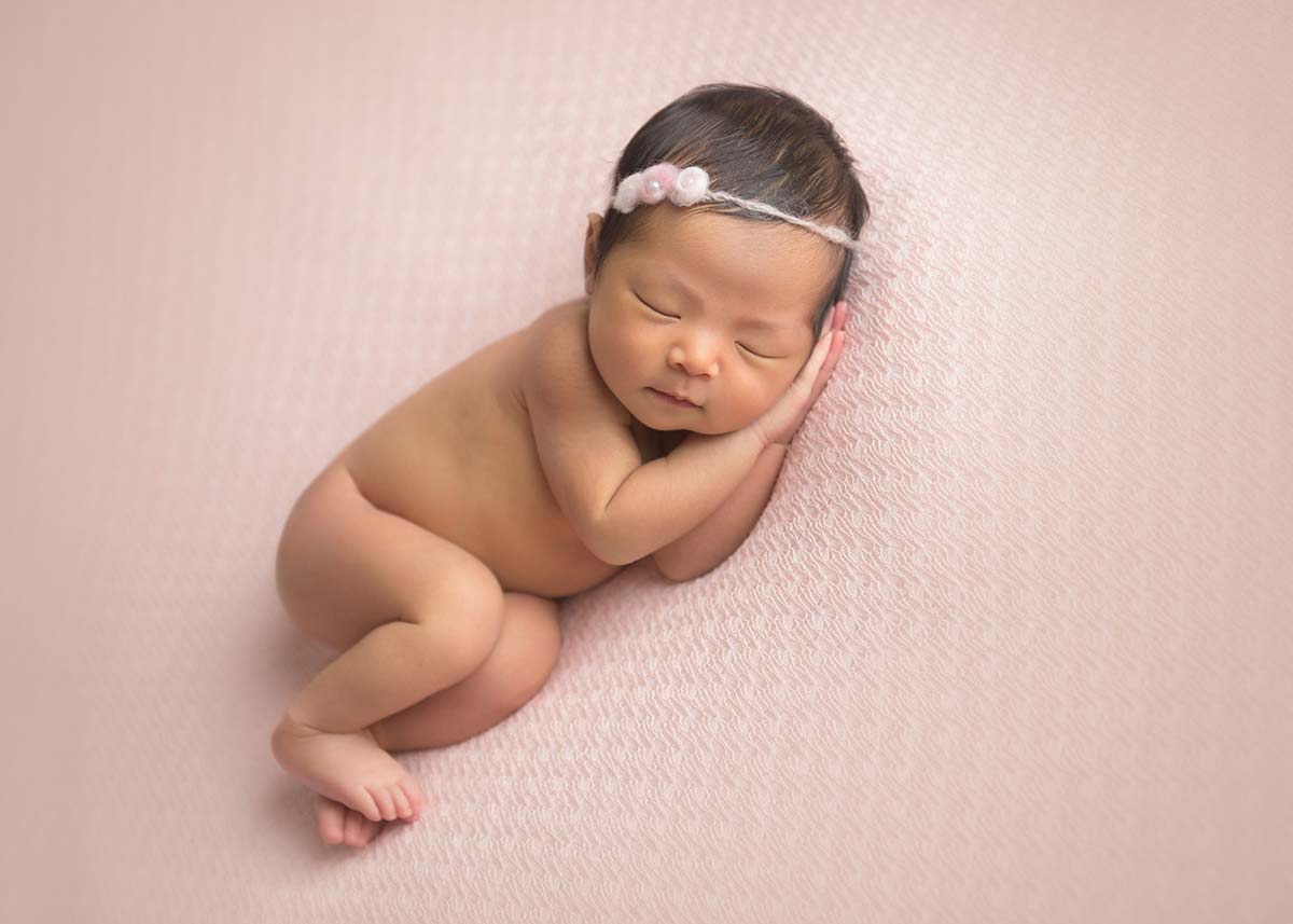 Newborn baby from Rye, NY laying on a pink blanket and posing for the newborn photographer.