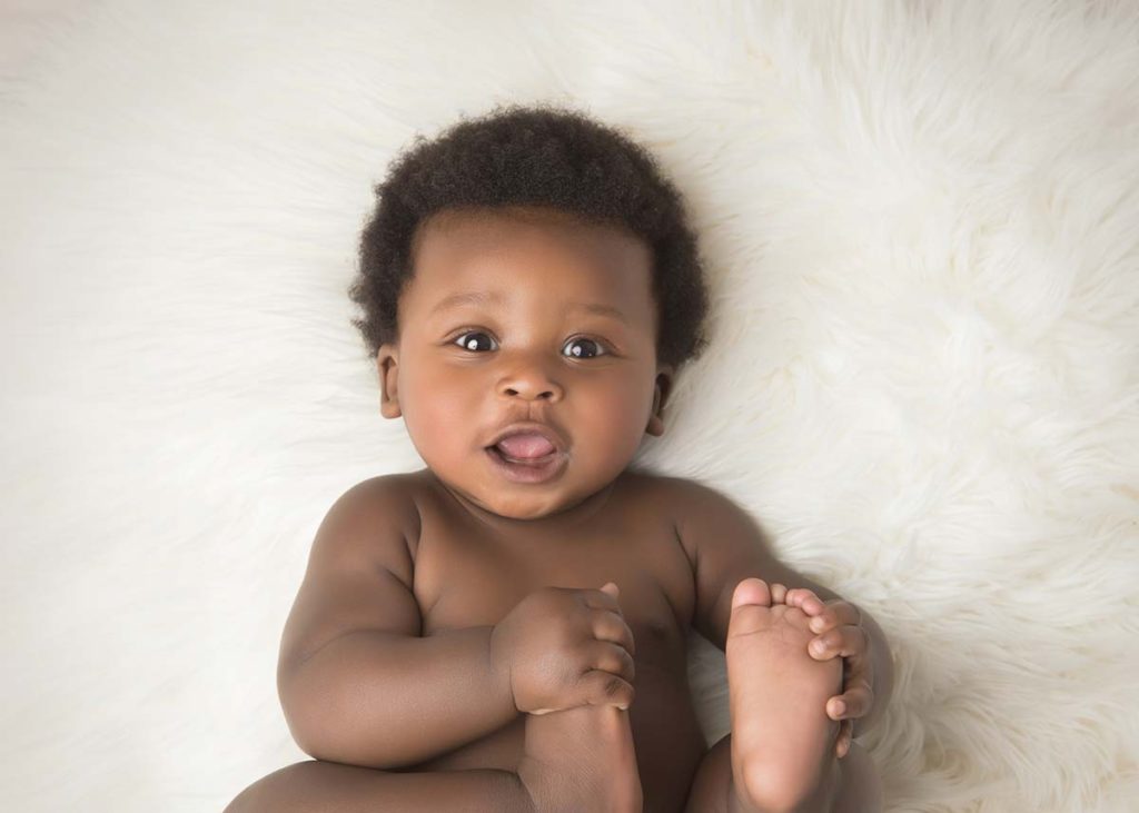 Classic baby photo of a boy holding his toes and smiling