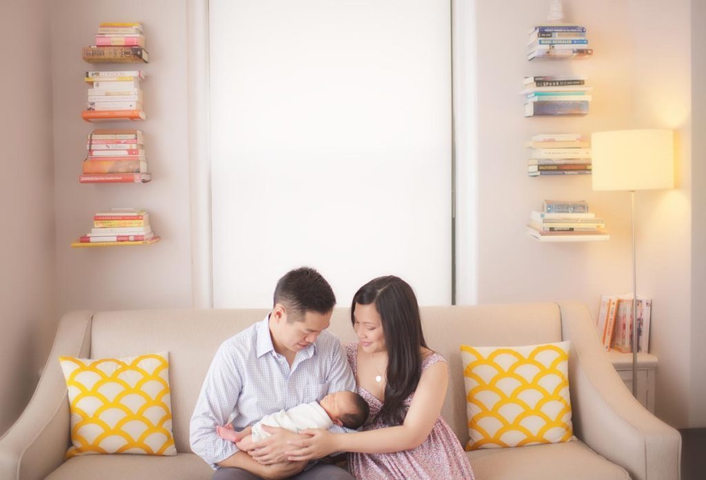 couch parents infant Attractive parents hold their newborn baby while posing for a photo in Westchester county