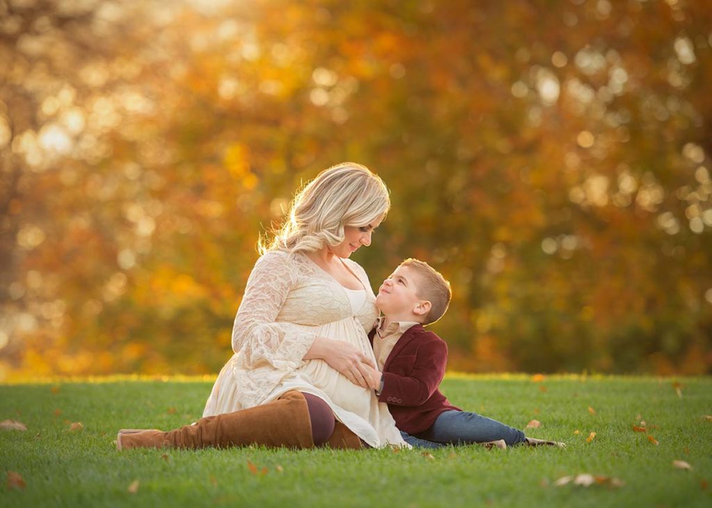 A pregnant mother and her son sitting in grass during the fall season in this Scarsdale NY park