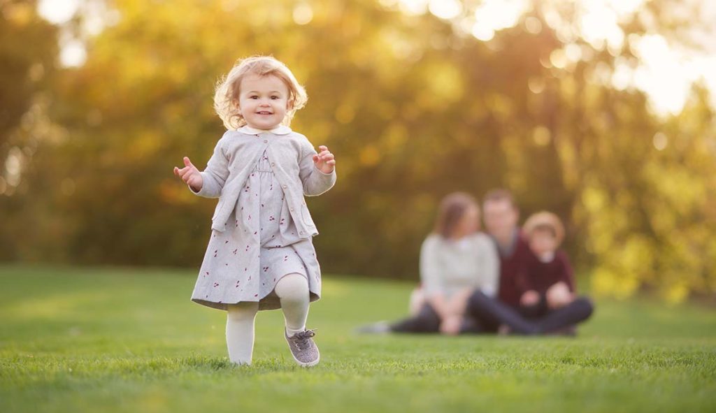 family portrait girl running Beautiful family photo of a girl running around her parents in a park in Connecticut