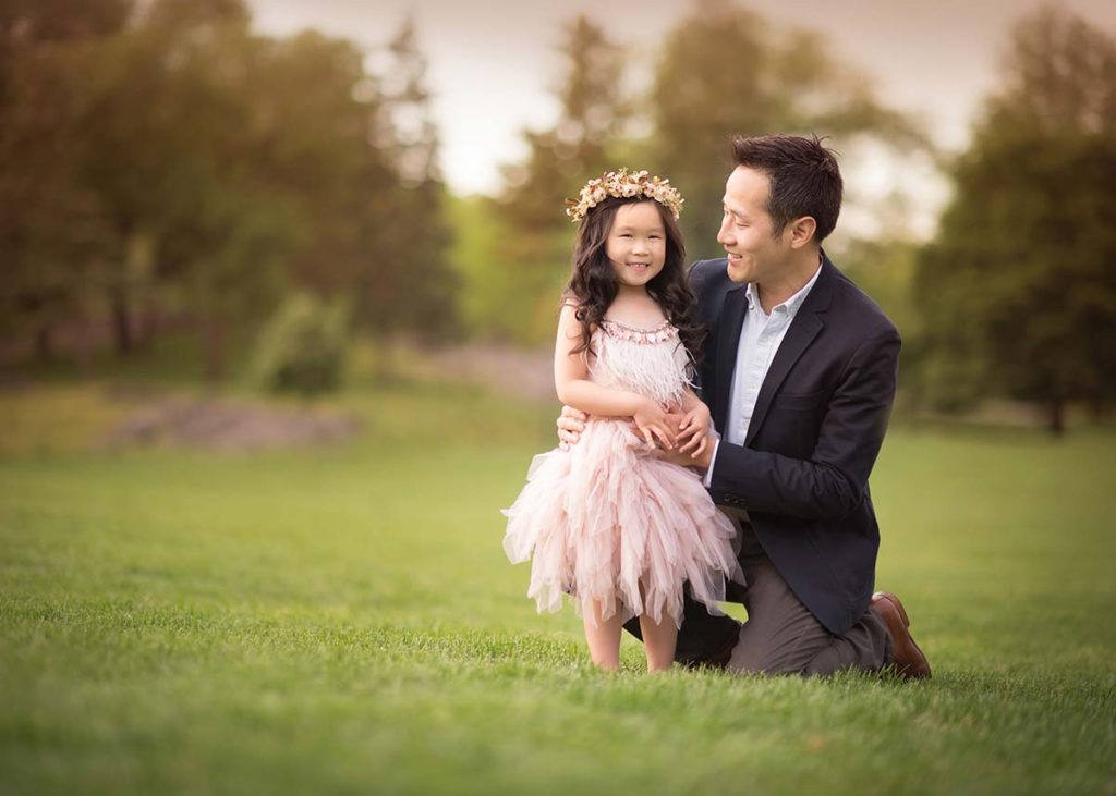 A proud father holding the hand of his young daughter wearing a tutu dress in a garden near Rye, NY.