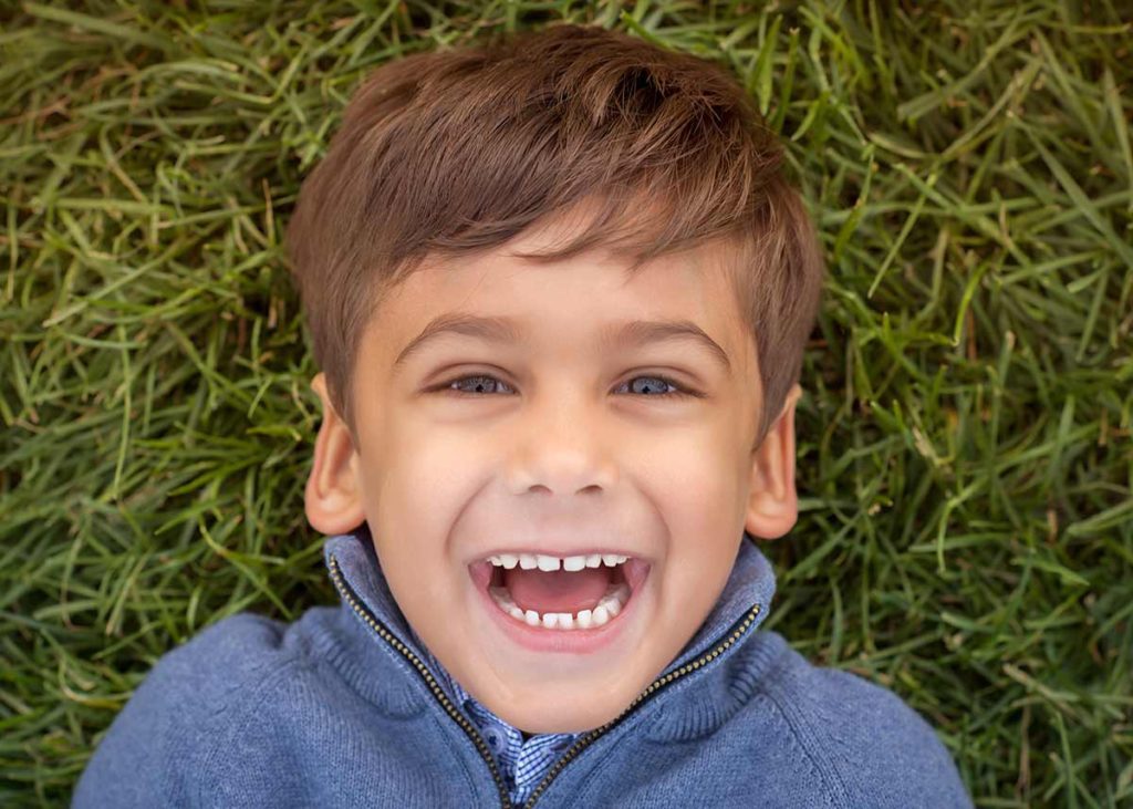 Boy laying in grass and staring up at the photographer laughing