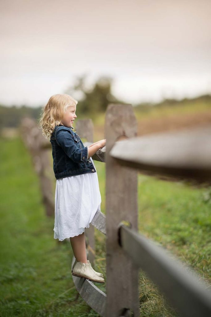 Priceless baby photo of a girl standing on a farm fence