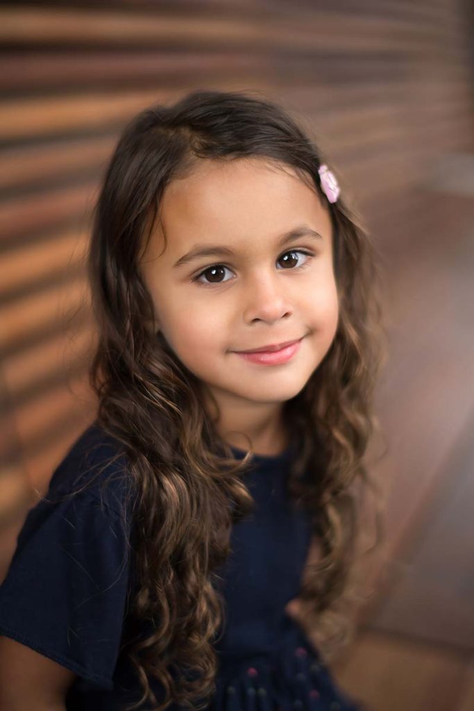 Girl with dark eyes and brown hair looking happily into the camera and smiling in this beautiful child photo