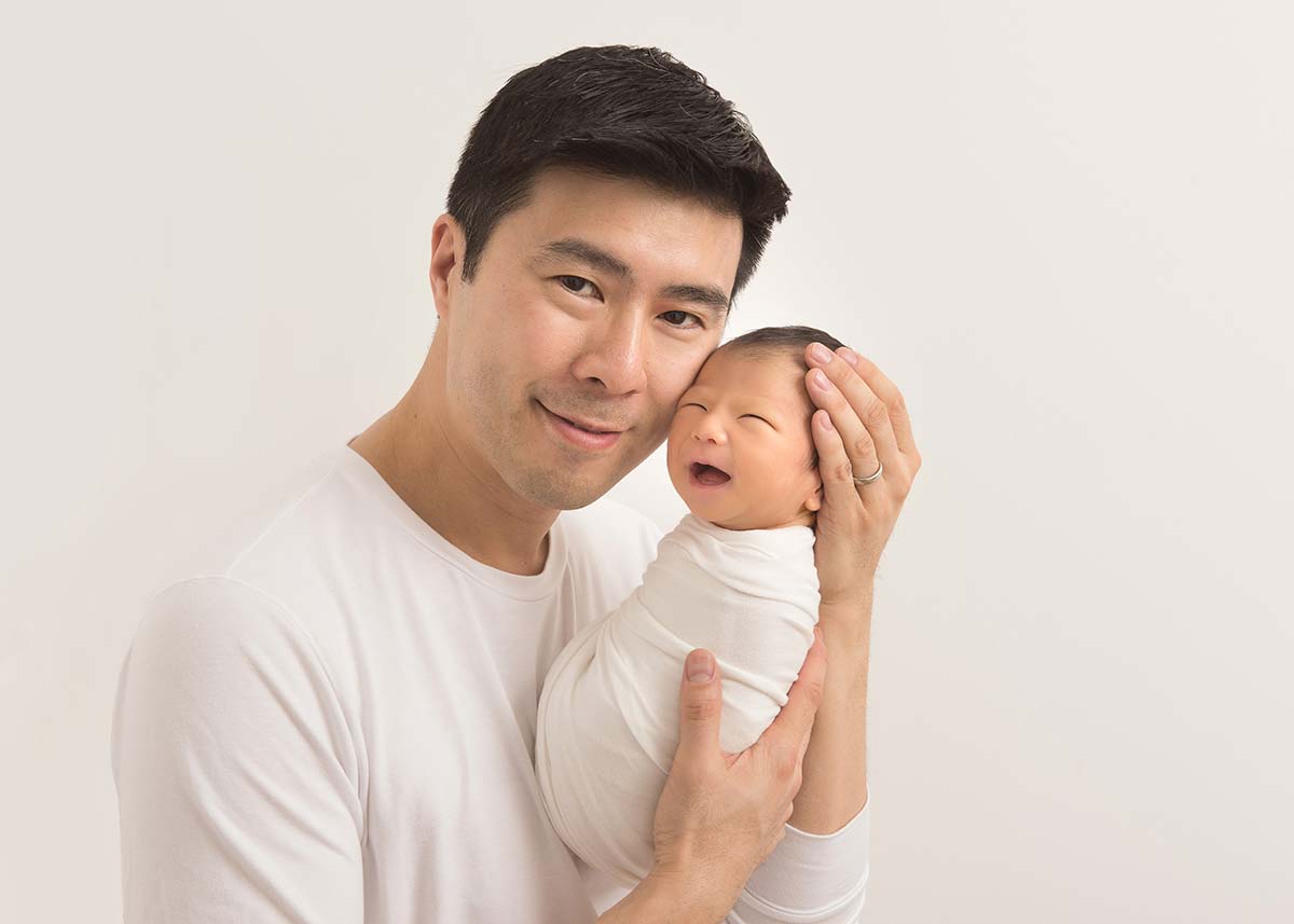 Happy father holding his newborn baby and posing for the newborn photographer.