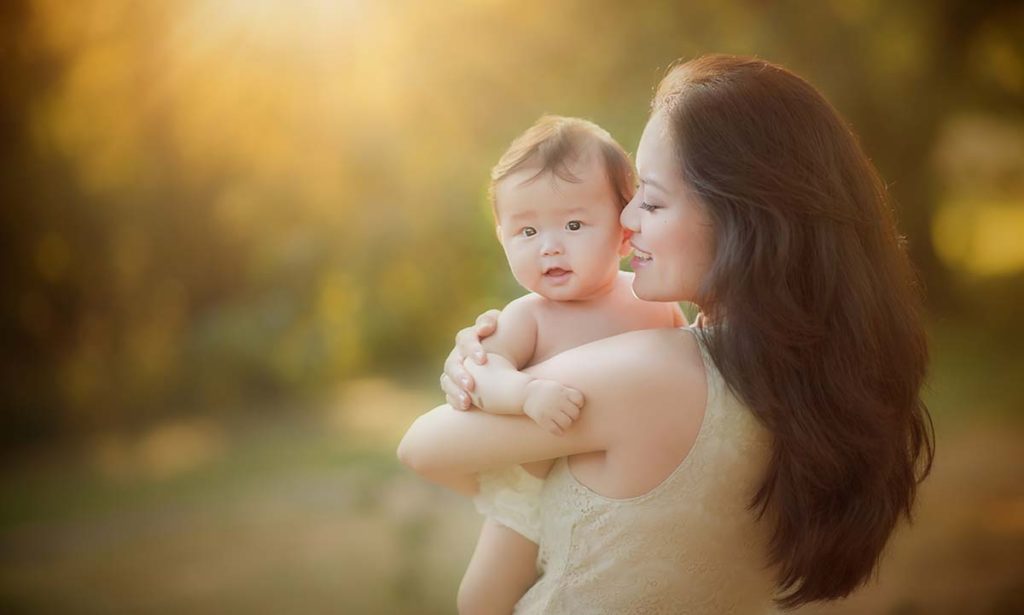 mother gently hugging baby Beautiful mother holding her baby during sunset