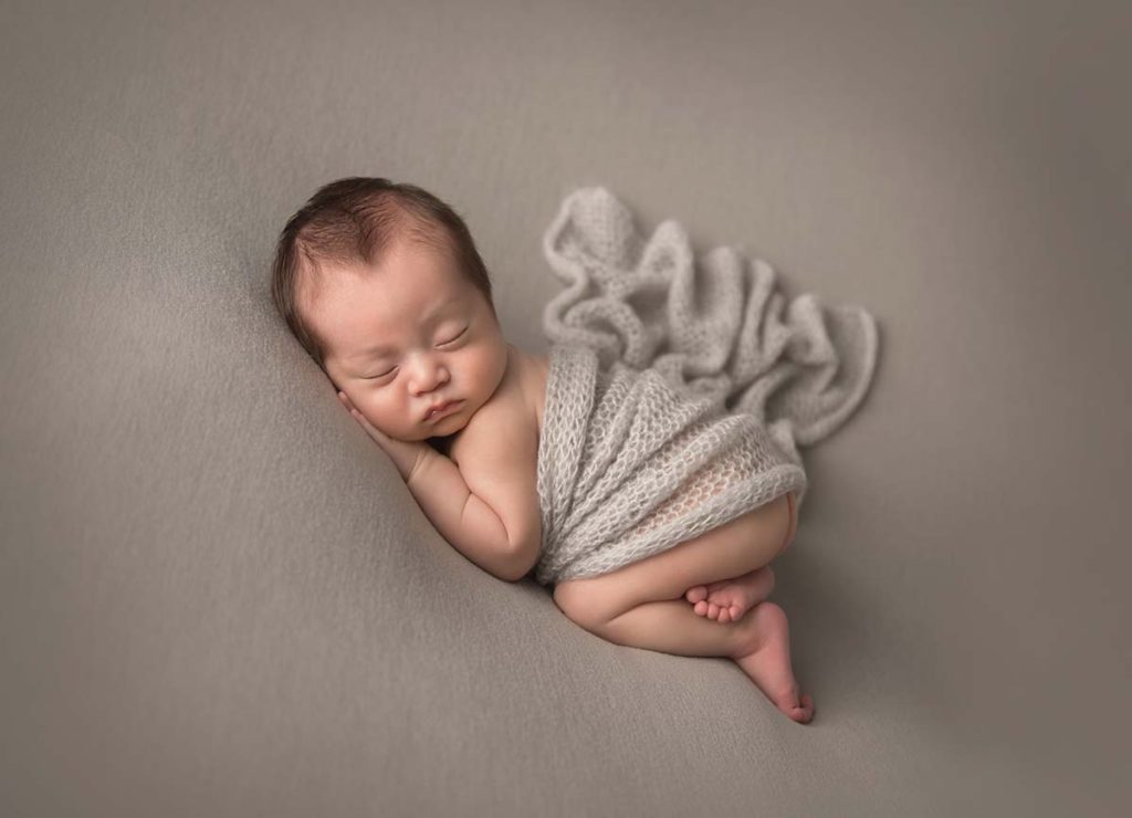 Professional newborn photographer captures this photo of a newborn baby happily sleeping on a blanket while wrapped in a knit swaddle.