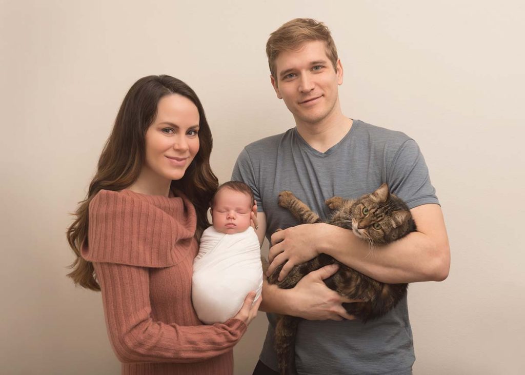 Parents smiling for a picture with their cat and baby