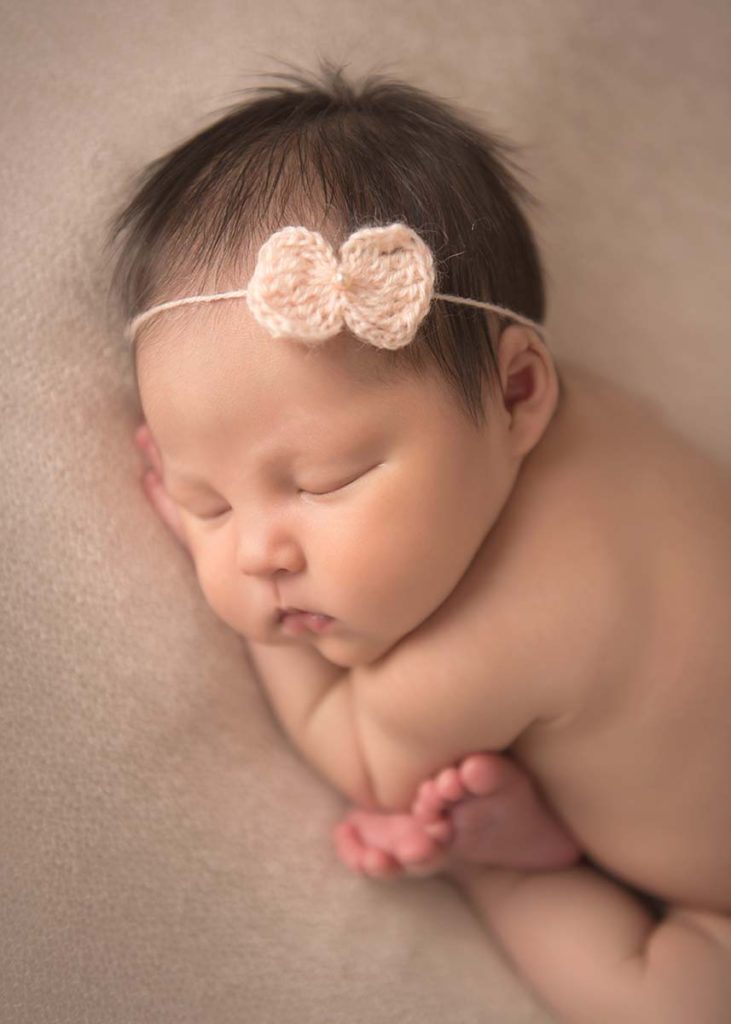 Infant baby with a headband and her feet curled up posing for the photographer