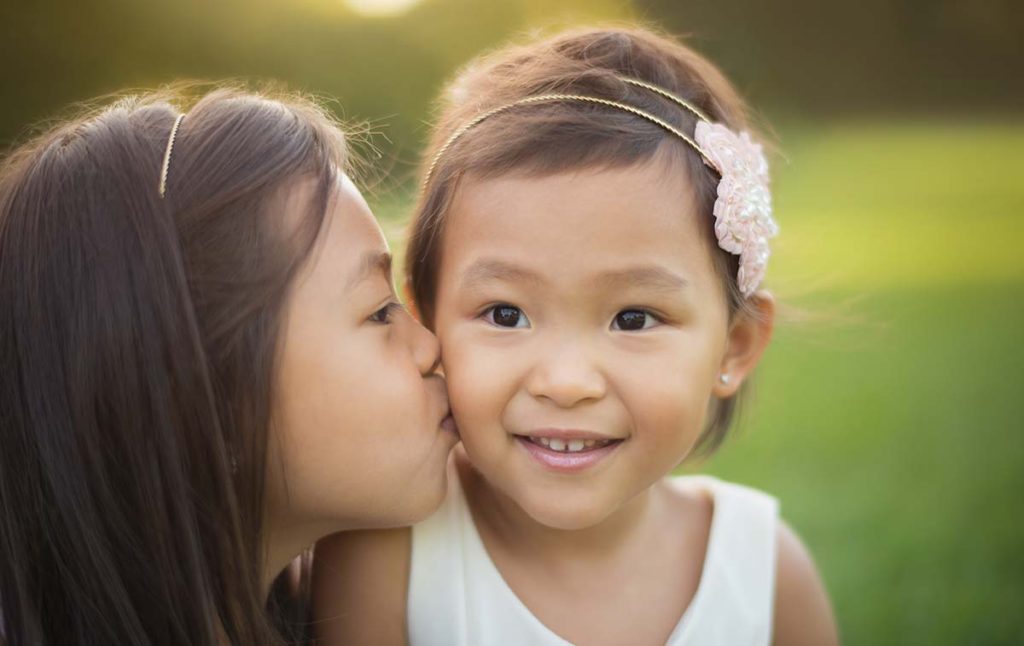 Two beautiful baby sisters kissing in this lifestyle baby photo