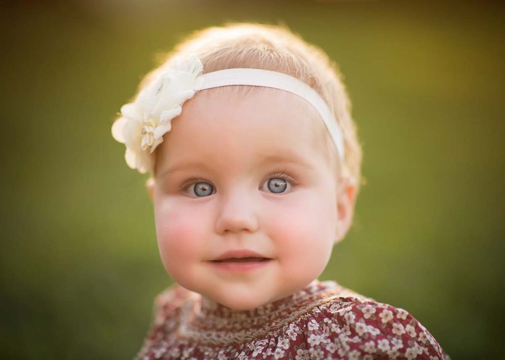 Baby girl with blue eyes and a headband smiles for the camera