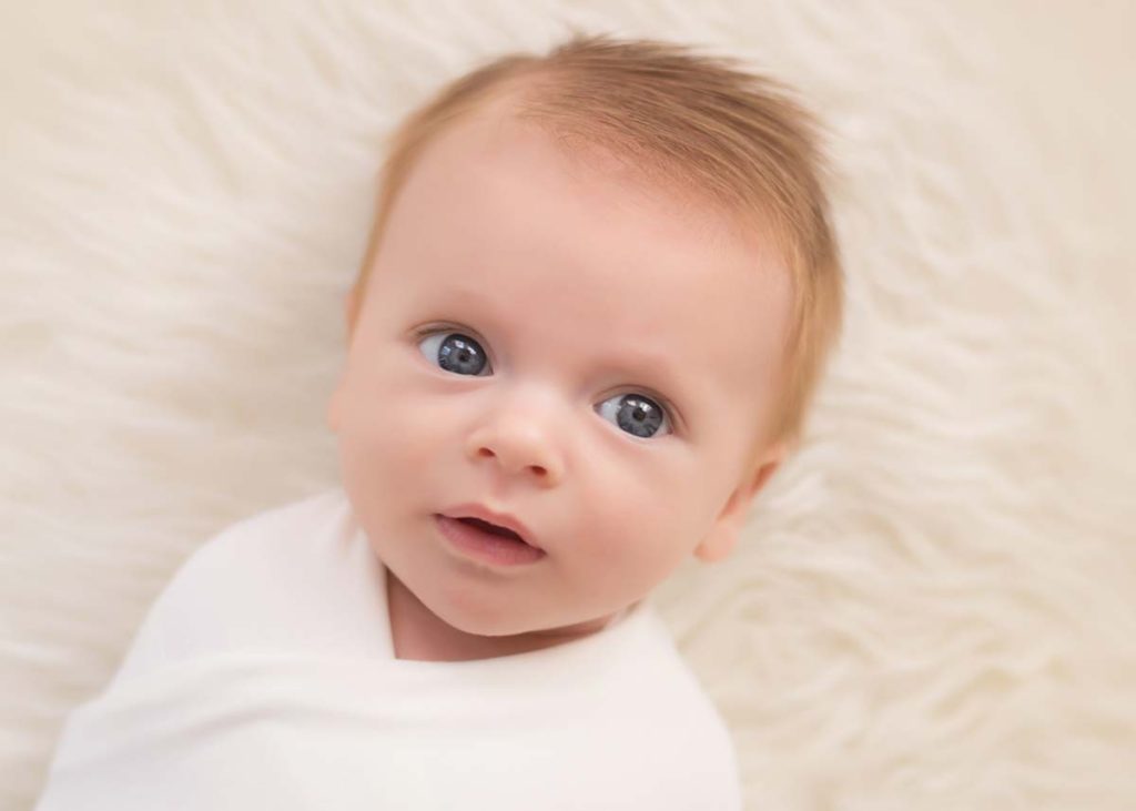 Baby with blue eyes smiling at the newborn photographer