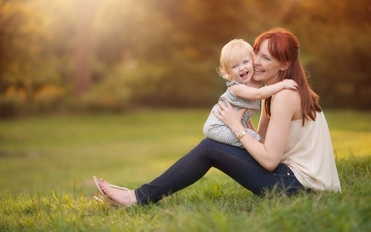 Mother with red hair kissing her beautiful daughter in a park