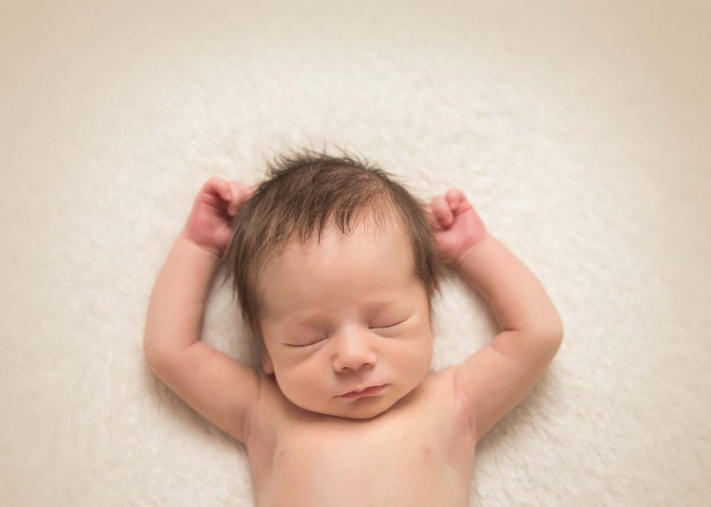 Newborn photographer poses a baby on his back with arms up in this relaxed photo