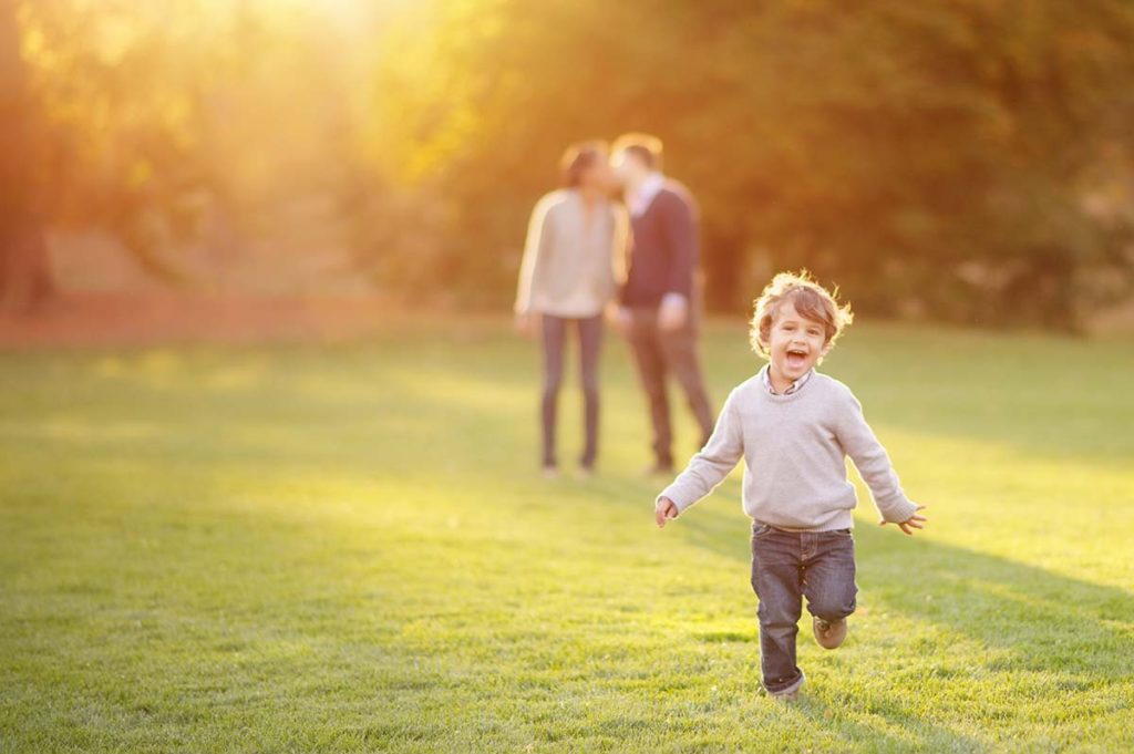 running boy family kissing Handsome boy smiling and running around his parents on a grass field near Greenwich, CT.