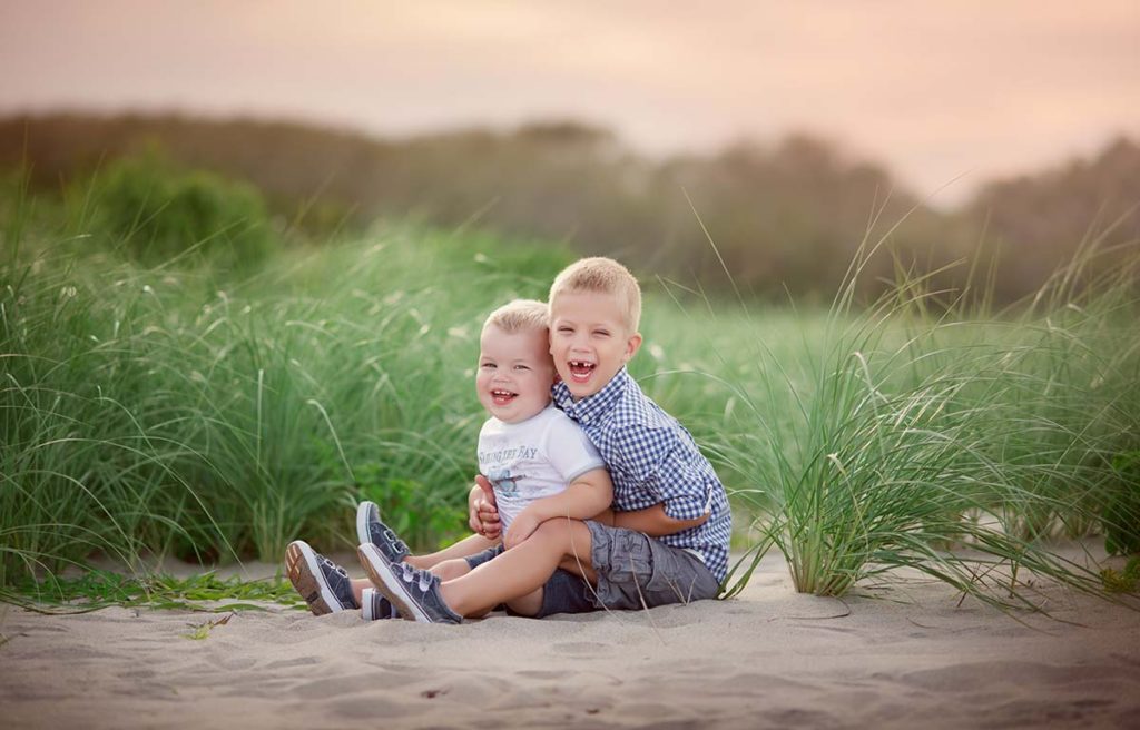 Two cute brothers with blonde hair hugging on a grassy beach near Norwalk, CT.