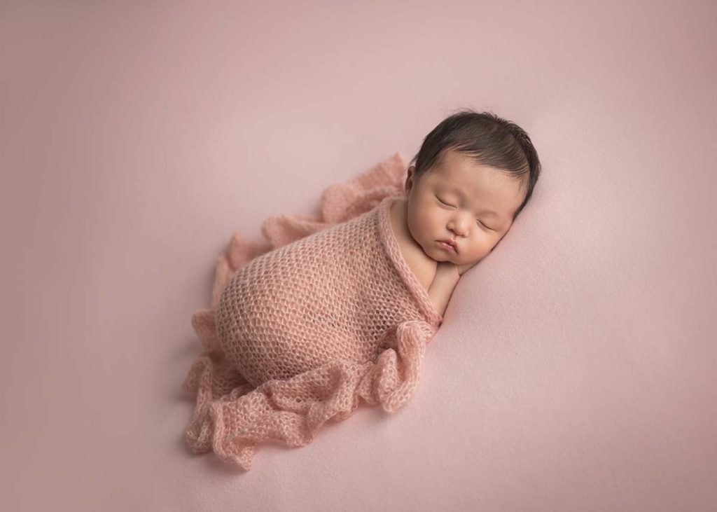 Baby girl in a pink wrap sleeping while posing for a newborn photo