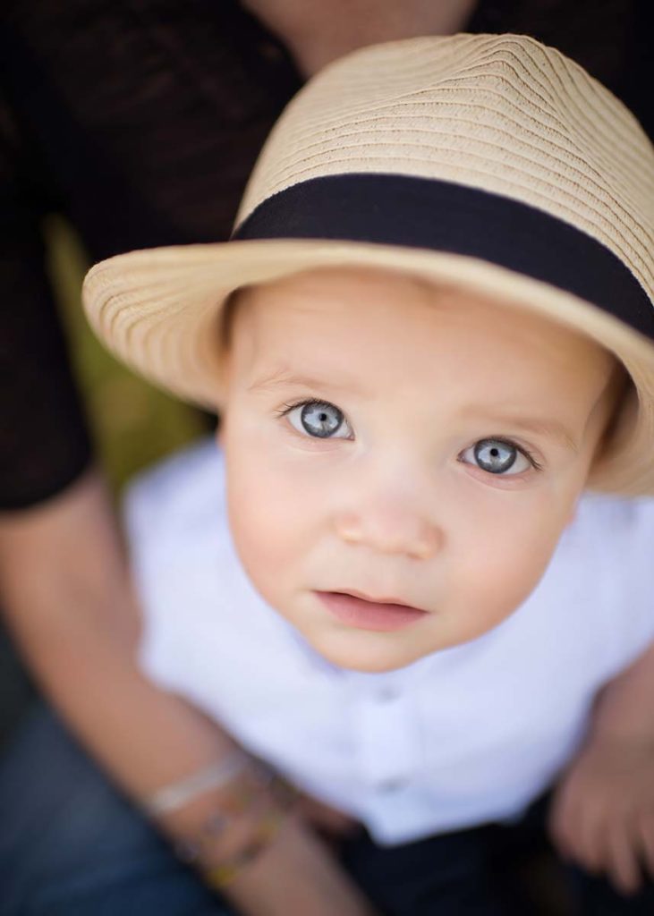 Toddler boy wearing a fedora hat and smiling at the photographer