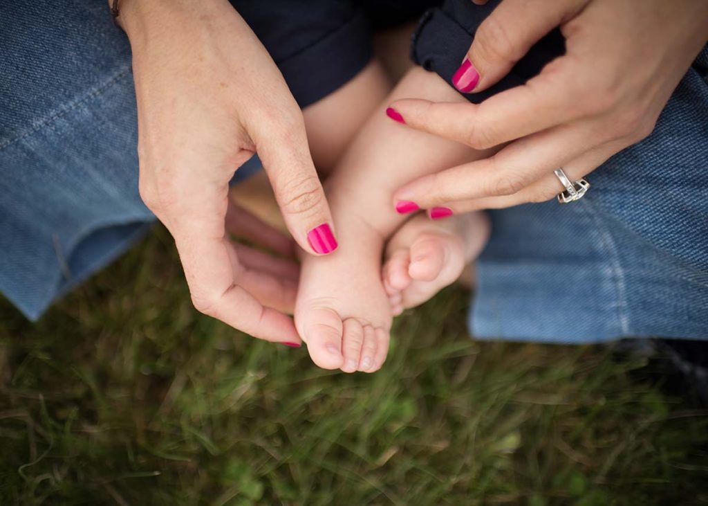 Closeup photo of a mother holding her baby's feet in the park