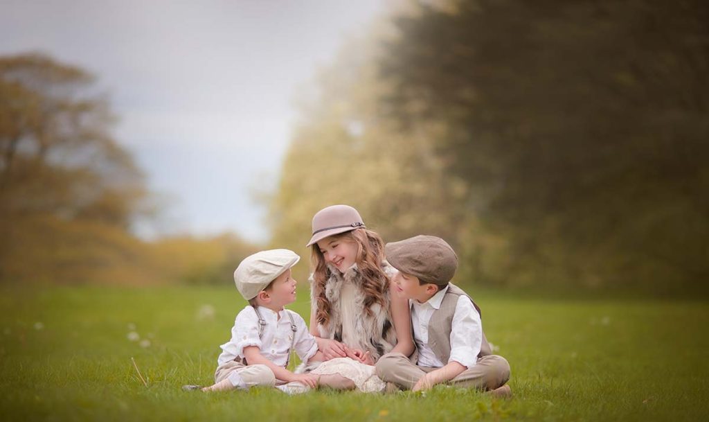 Three beautiful children wearing hats and stylish clothes smiling together in a grass field in Greenwich CT.