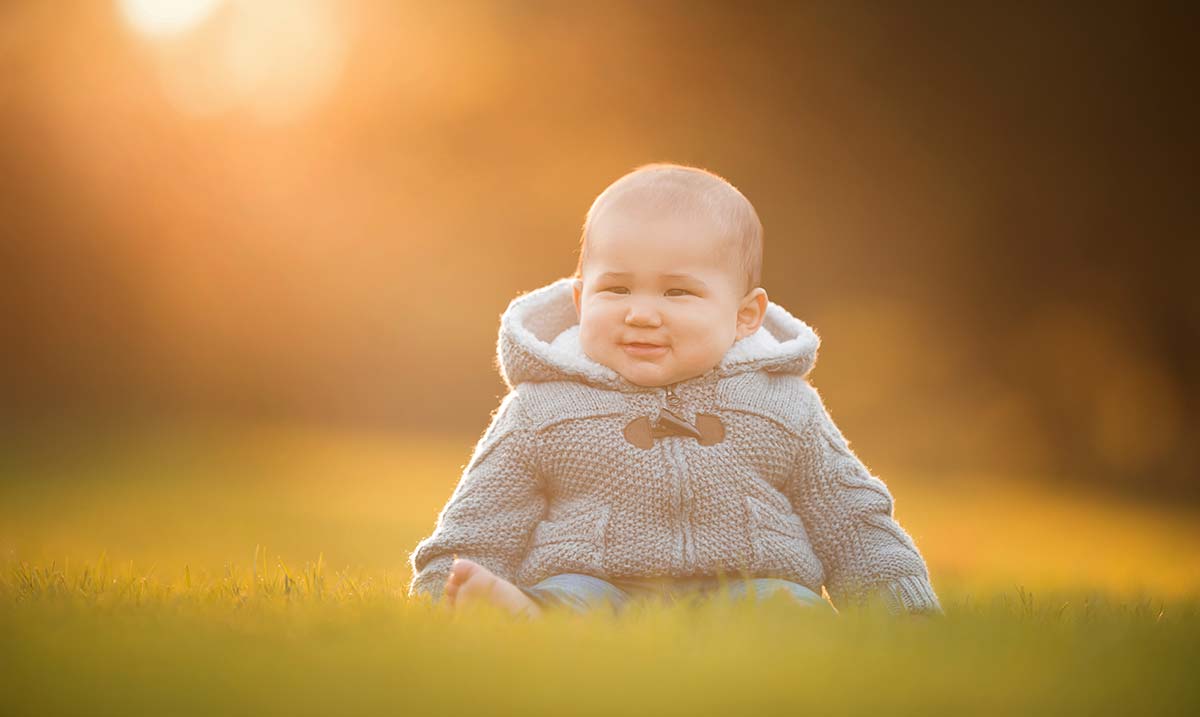 Boy in a winter hoodie sitting in grass in this beautiful sunset photo
