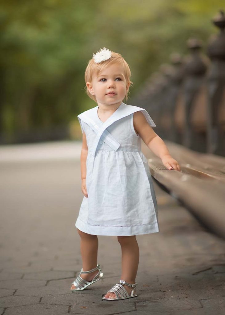 Pretty little girl wearing a dress and holding onto a bench
