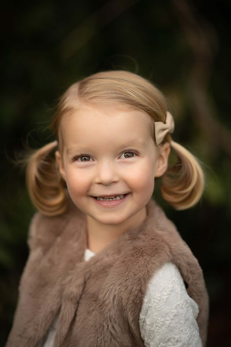 Young blonde girl with pigtails smiling at the baby photographer
