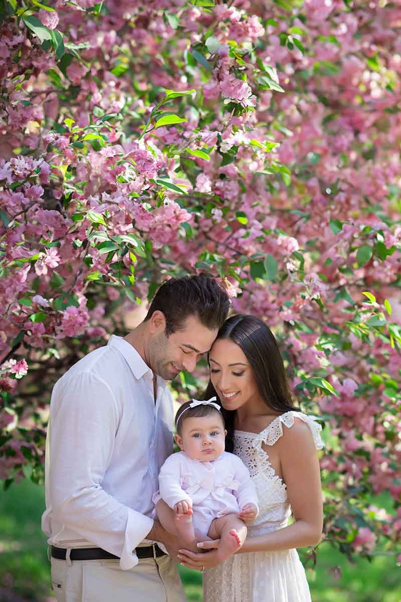 Portrait of couple standing together with baby amidst cherry blossoms