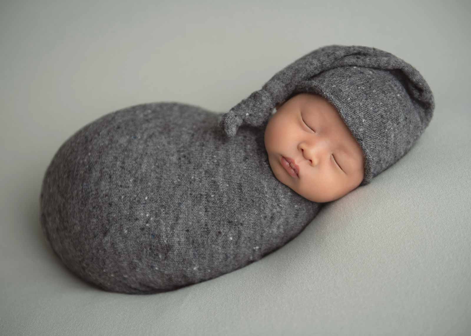Newborn baby swaddled in gray sleeping peacefully